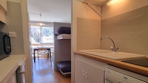 Una cocina compacta con un lavamanos, estufa y un comedor visible a través de una puerta abierta.
