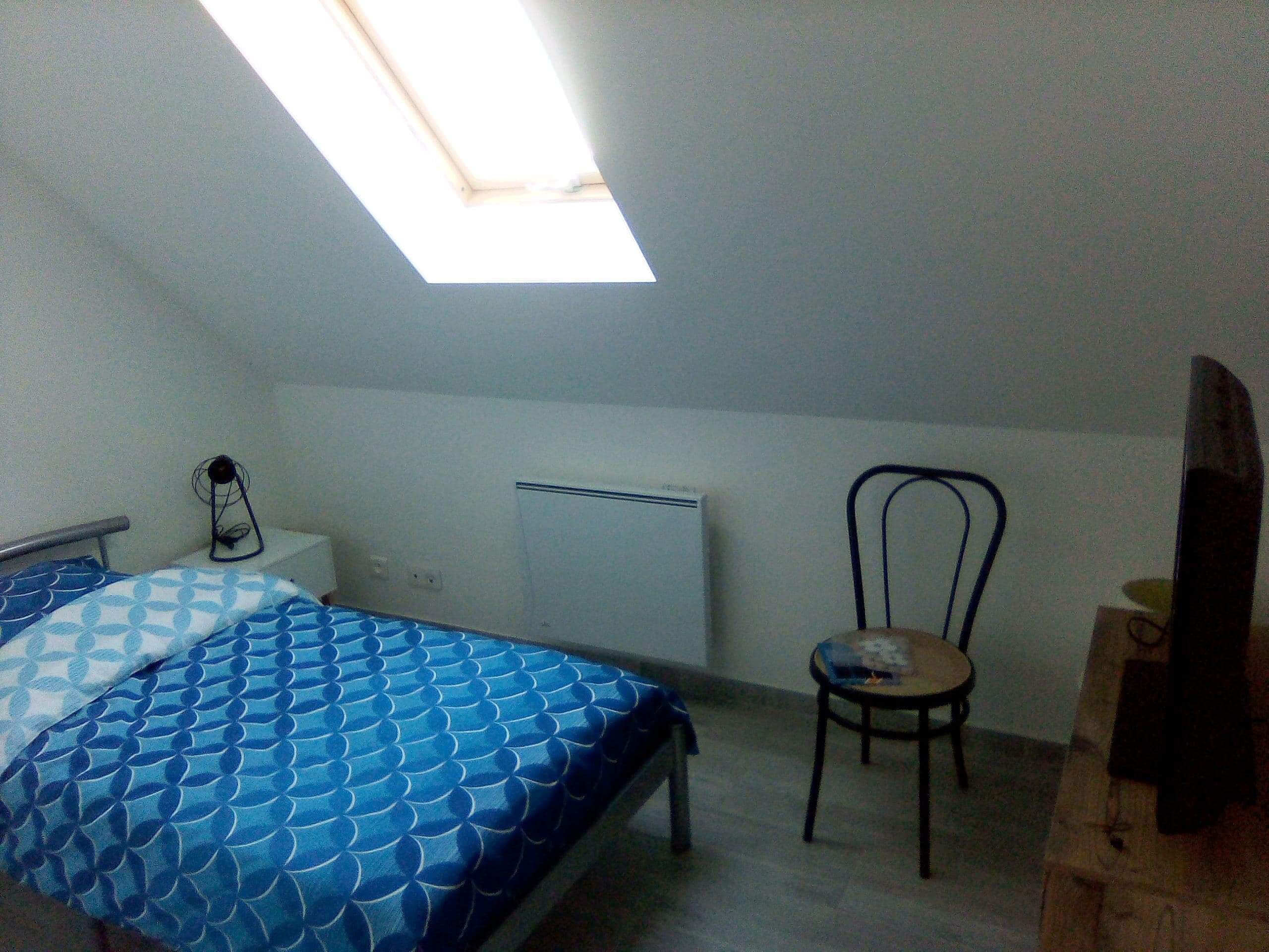 A small, simple room with a bed, a chair, a desk, and a radiator.