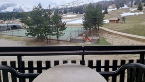 A view from a balcony overlooking a tennis court, a playground, and a mountainous landscape with snow-covered peaks.