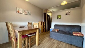 A cozy room with a wooden dining table, chairs, a sofa, and a small kitchenette.