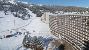A large hotel with multiple floors, surrounded by snow-covered trees and a ski slope.