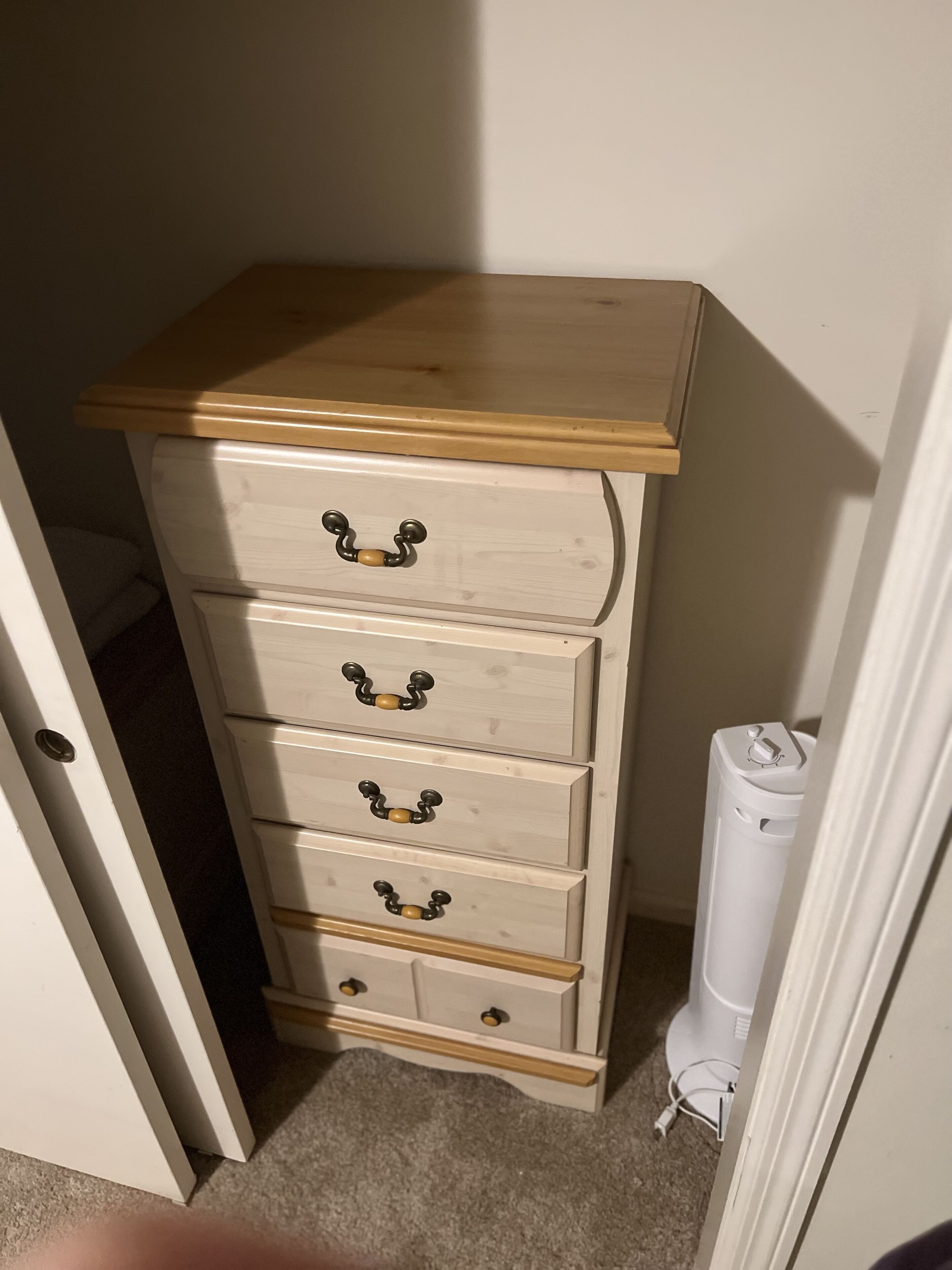 Ein weißer Kommode mit Holzbeschlag und vier Schubladen, jede mit einem schwarzen Griff.