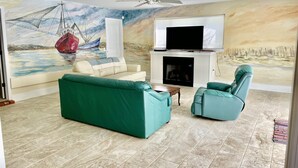 Un salon orné d’une fresque représentant un voilier, avec une cheminée et un téléviseur posé sur un meuble.