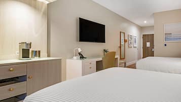 Habitación de hotel con dos camas, un escritorio con silla, un televisor de pantalla plana, cafetera y un cuadro en la pared.