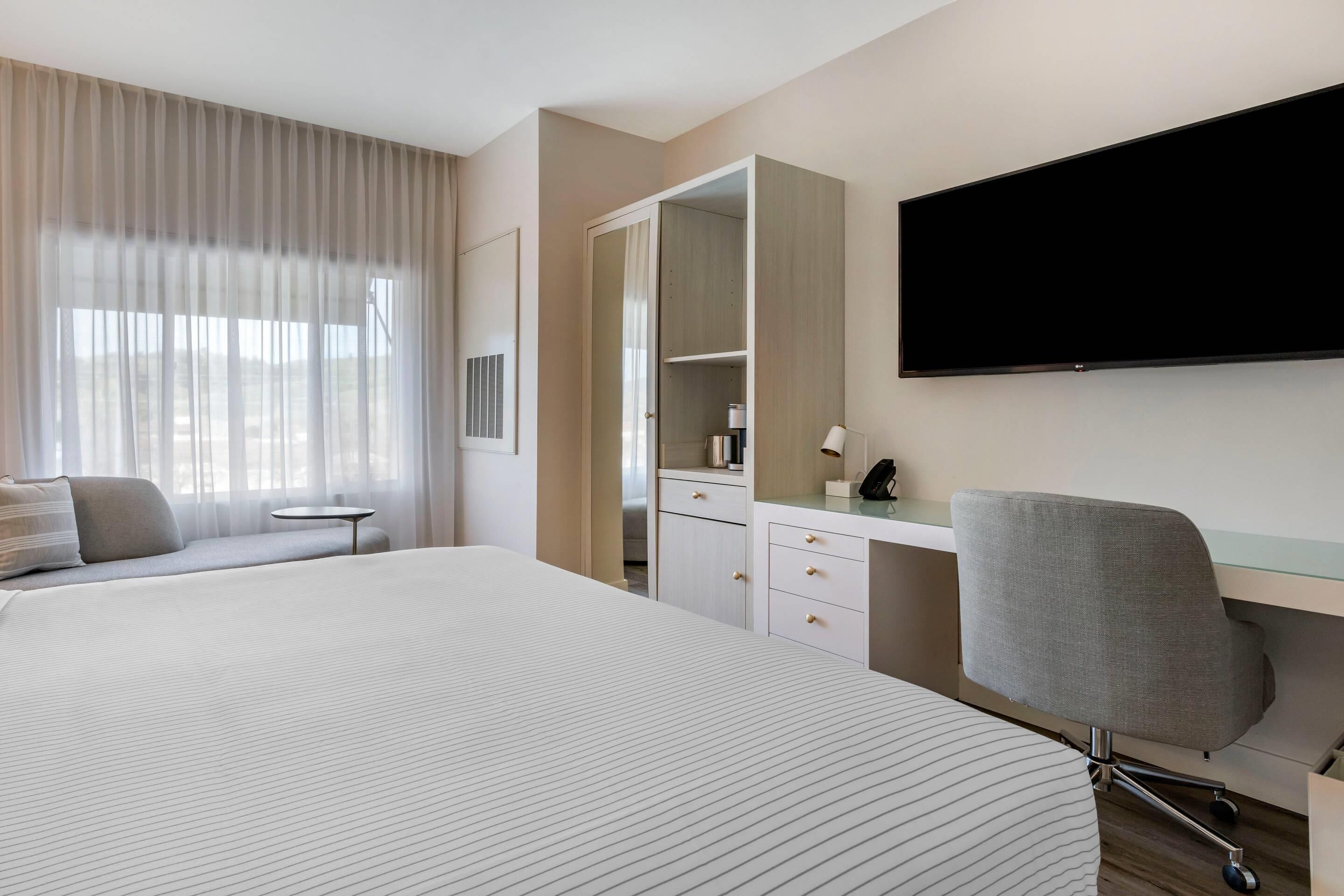 Una camera d'albergo con un letto grande, una scrivania con una sedia, un armadio e una TV a schermo piatto.