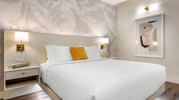 A modern hotel room with a large bed, two bedside tables with lamps, a wall mural, and a framed abstract artwork.