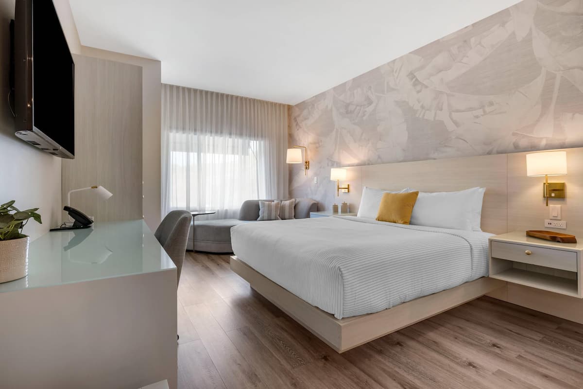 Una habitación de hotel moderna con una cama grande, un escritorio, una silla, un televisor y una pared con diseño tipo mármol.