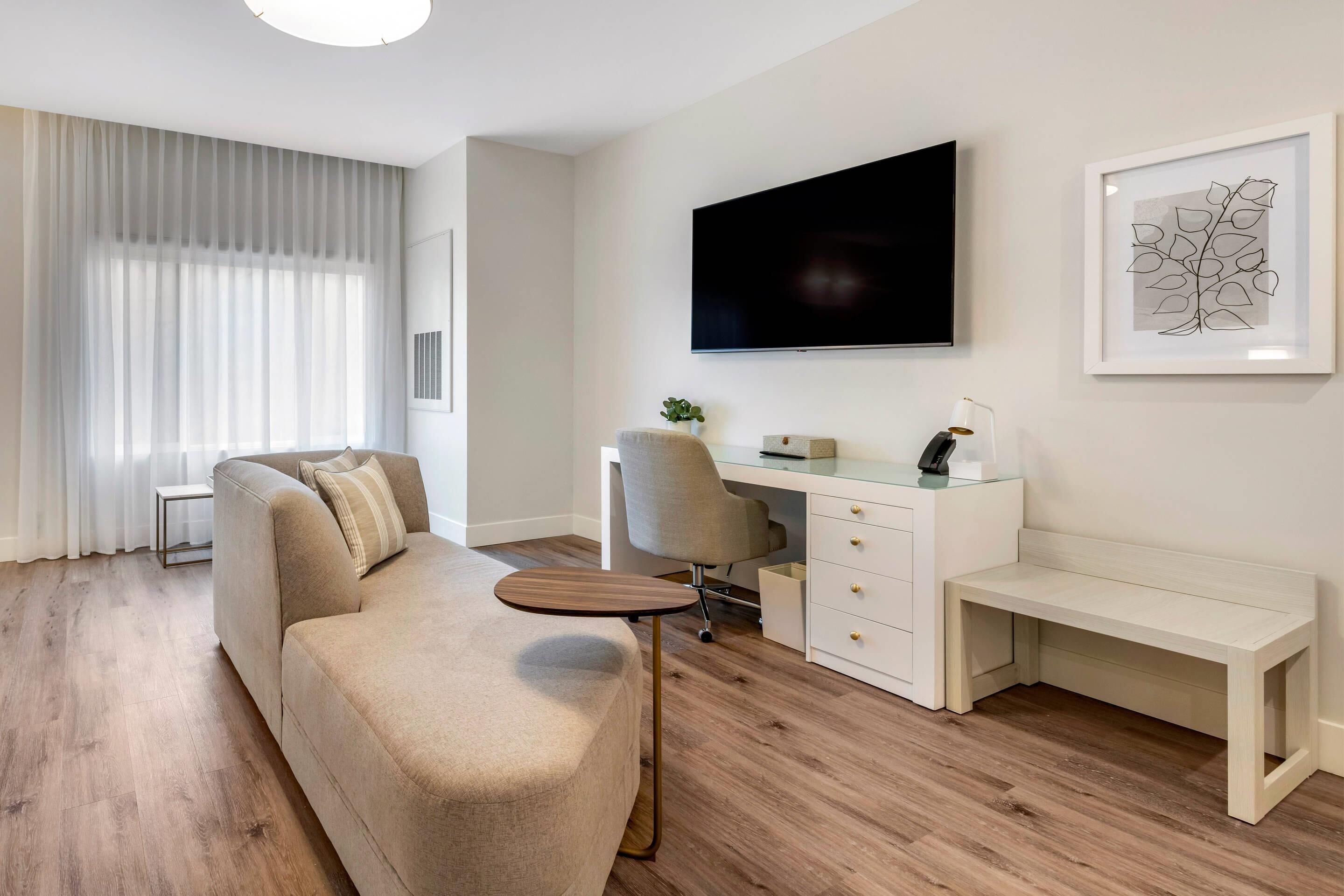 A modern living room with a sofa, a desk, a chair, and a TV mounted on the wall.