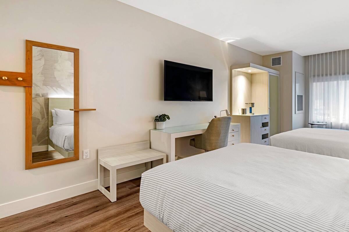 Habitación de hotel con dos camas, un escritorio, una silla, un televisor y un espejo.