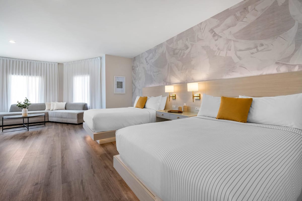 Habitación de hotel con dos camas, un sofá, una mesita de centro y un mural abstracto de gran tamaño en la pared.