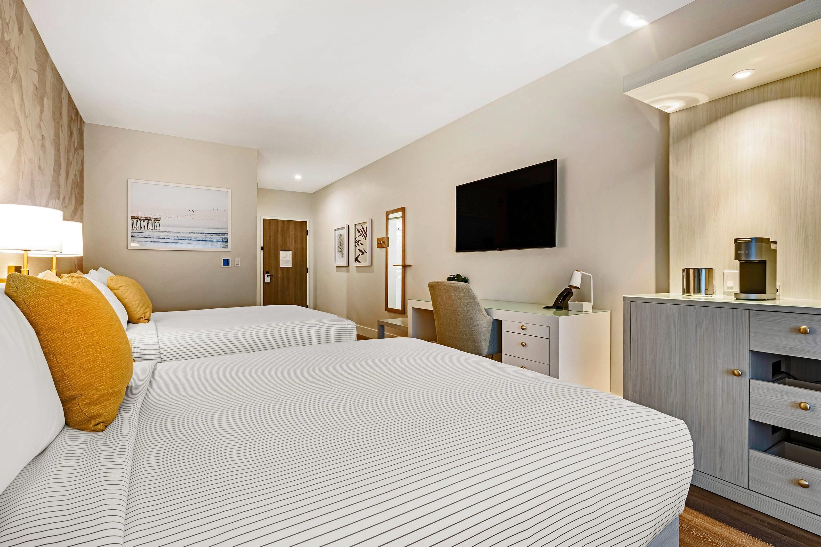 Habitación de hotel con dos camas, un escritorio, una silla, un televisor de pantalla plana y un minibar.