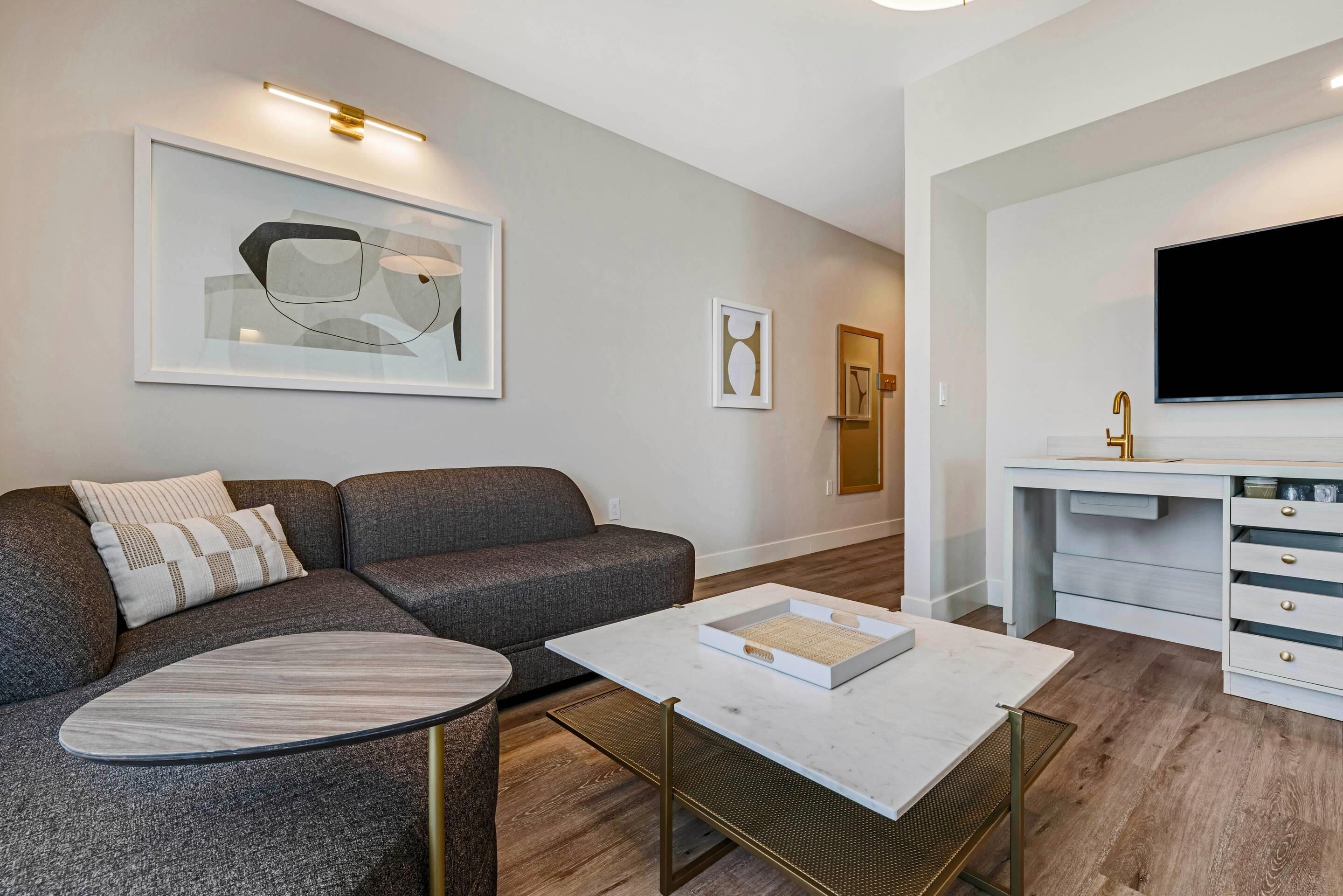 Un salon moderne avec un canapé d’angle, une table basse, un téléviseur fixé au-dessus d’un meuble blanc et des œuvres d’art encadrées accrochées aux murs.