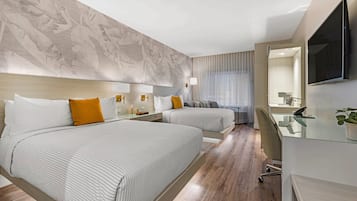 A hotel room with two beds, a desk, a chair, a TV, and a large window with curtains.
