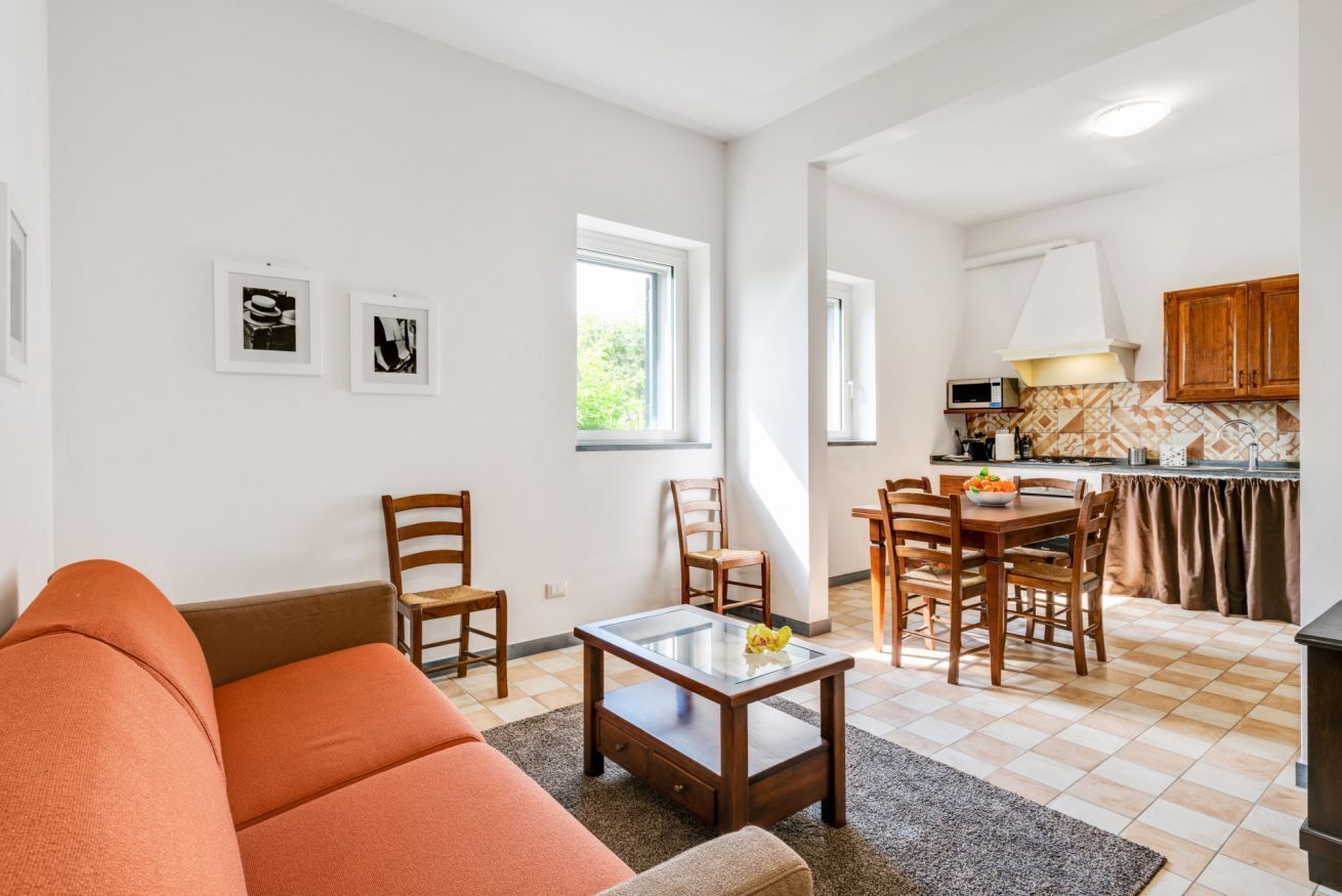 Ett vardagsrum med en soffa, fåtöljer och ett soffbord, samt en köksdel med ett matbord och stolar.