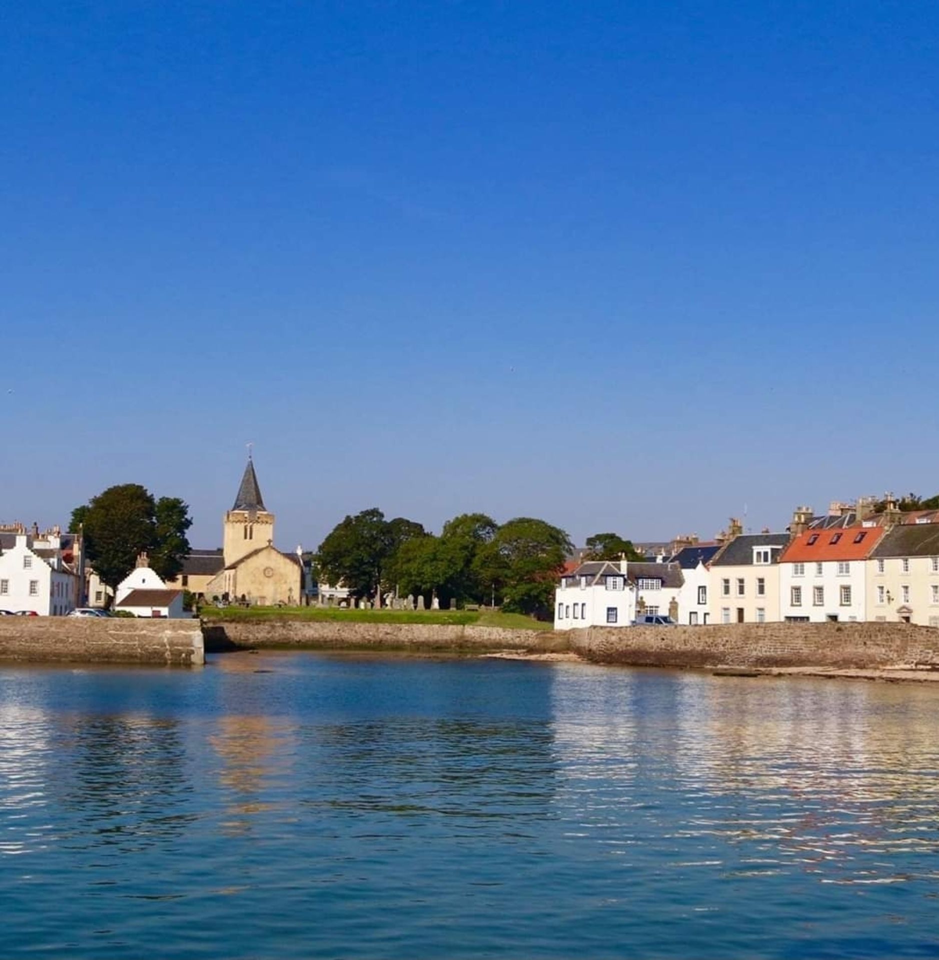 A waterfront view with a church, white buildings, and a stone wall.