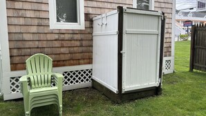 A wooden house with a white garage door, a green plastic chair, and a white fence. - Charming 2-bedroom cottage in Old Orchard Beach, perfect for family getaways. (Old Orchard Beach)