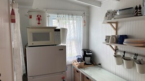 A compact kitchen with a microwave on top of a refrigerator, a coffee maker, and a shelf with dishes and utensils. - Charming 2-bedroom cottage in Old Orchard Beach, perfect for family getaways. (Old Orchard Beach)