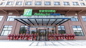 Eingangsbereich eines Holiday Inn Express Hotels mit Glasüberdachung, zahlreichen Fenstern und floralen Dekorationen.