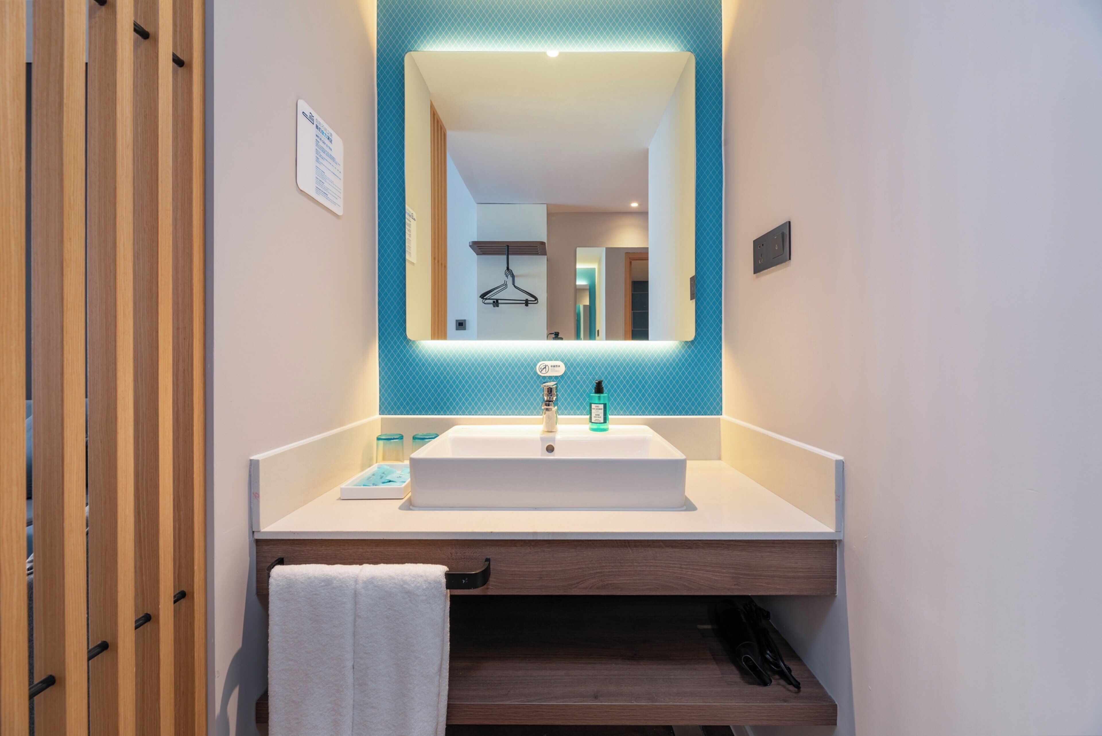 Une salle de bain moderne avec un lavabo blanc, un miroir agrémenté d’une touche de bleu et un porte-serviettes.