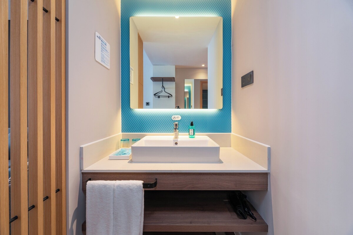 A modern bathroom with a large mirror, white sink, and wooden vanity.