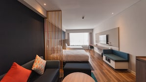 Ein modernes Hotelzimmer mit einer Couch, zwei Betten, einem Schreibtisch und einem großen Fenster.