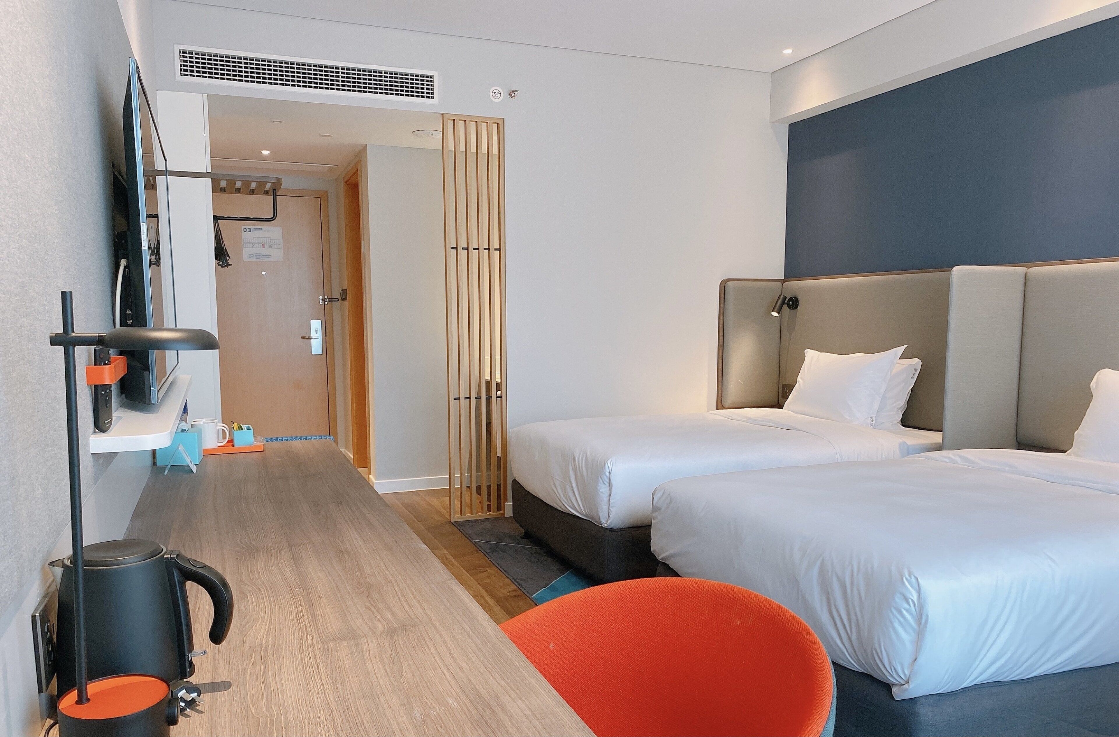 Habitación de hotel con dos camas, un escritorio con hervidor, una silla y un televisor.