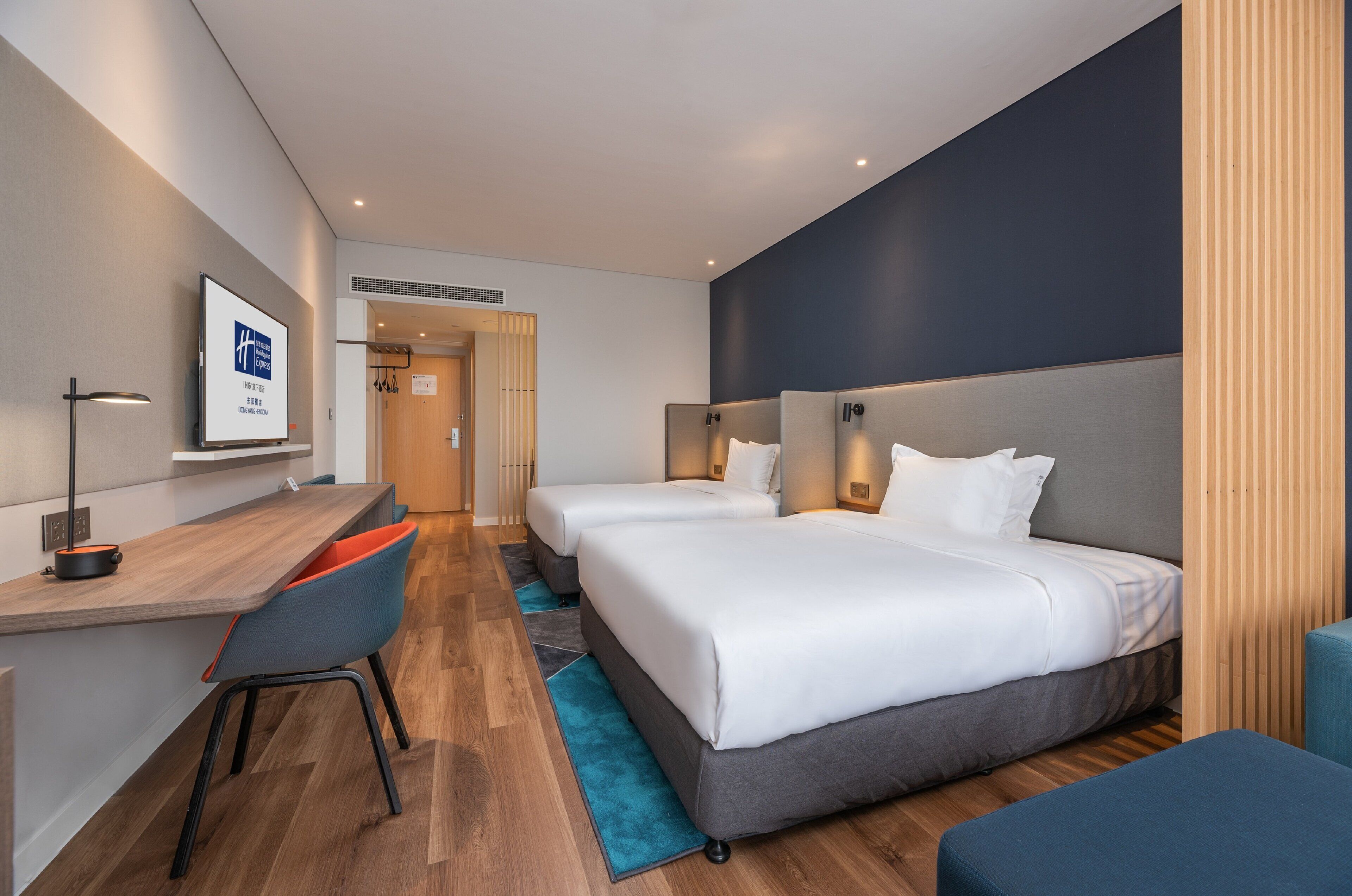 Habitación de hotel con dos camas, un escritorio, sillas y una televisión.