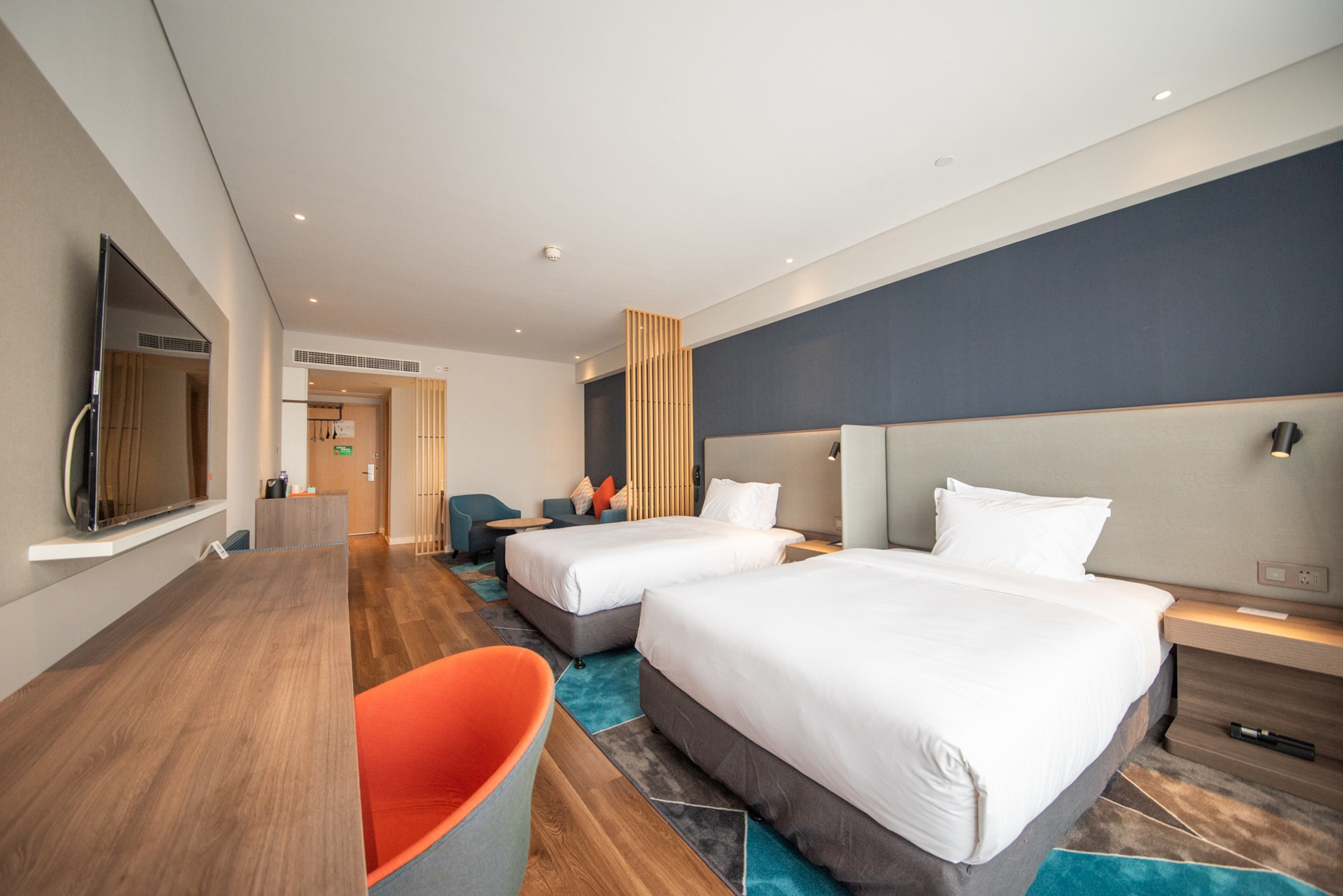 A hotel room with two beds, a desk, a chair, and a television.