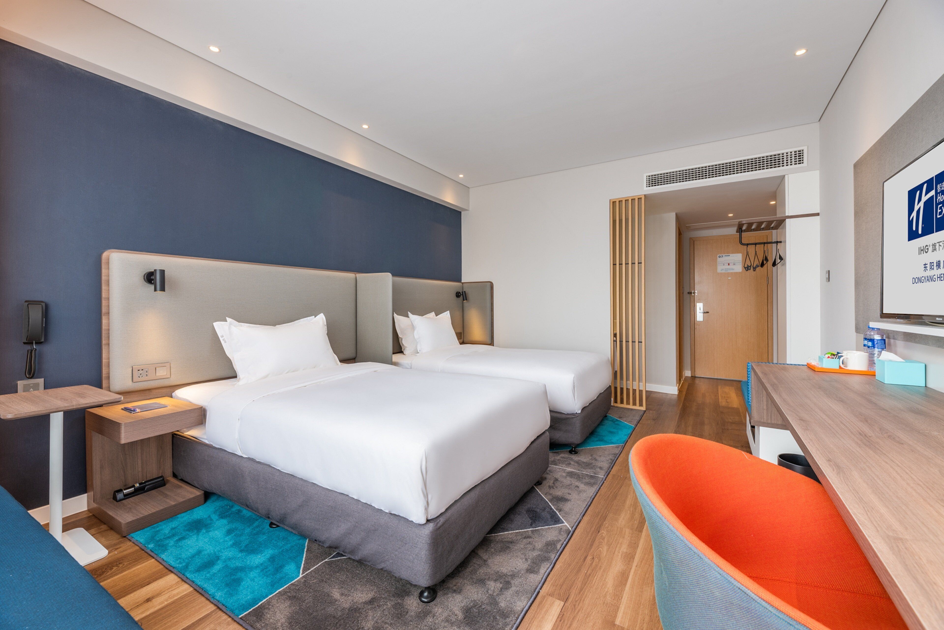 A modern hotel room with two beds, a desk, and a seating area.