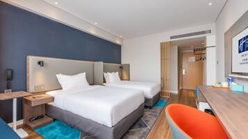 A modern hotel room with two beds, a desk, and a seating area.