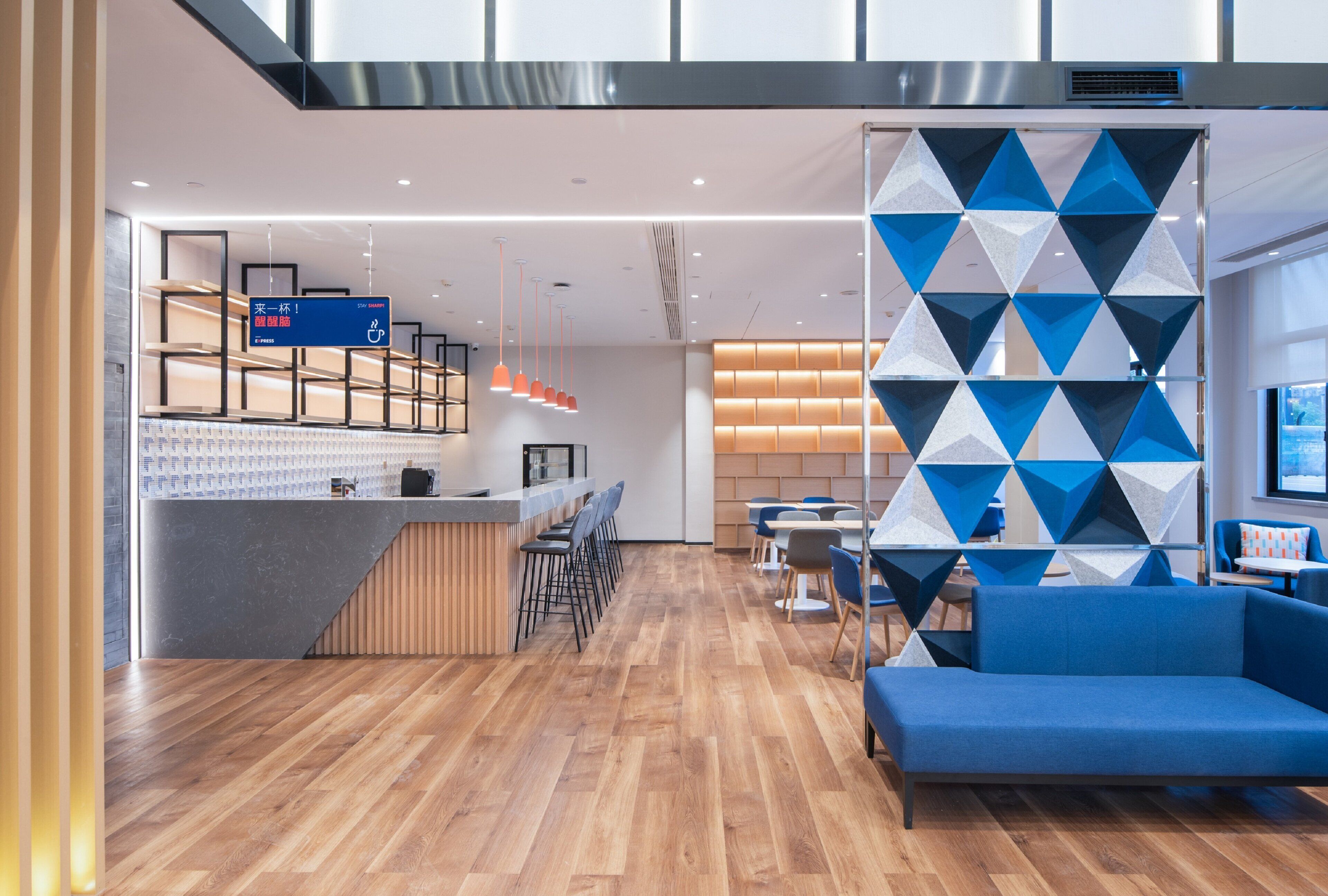 Un moderno vestíbulo de hotel con suelo de madera, un mostrador de recepción, zona de estar y una pared con motivo geométrico.