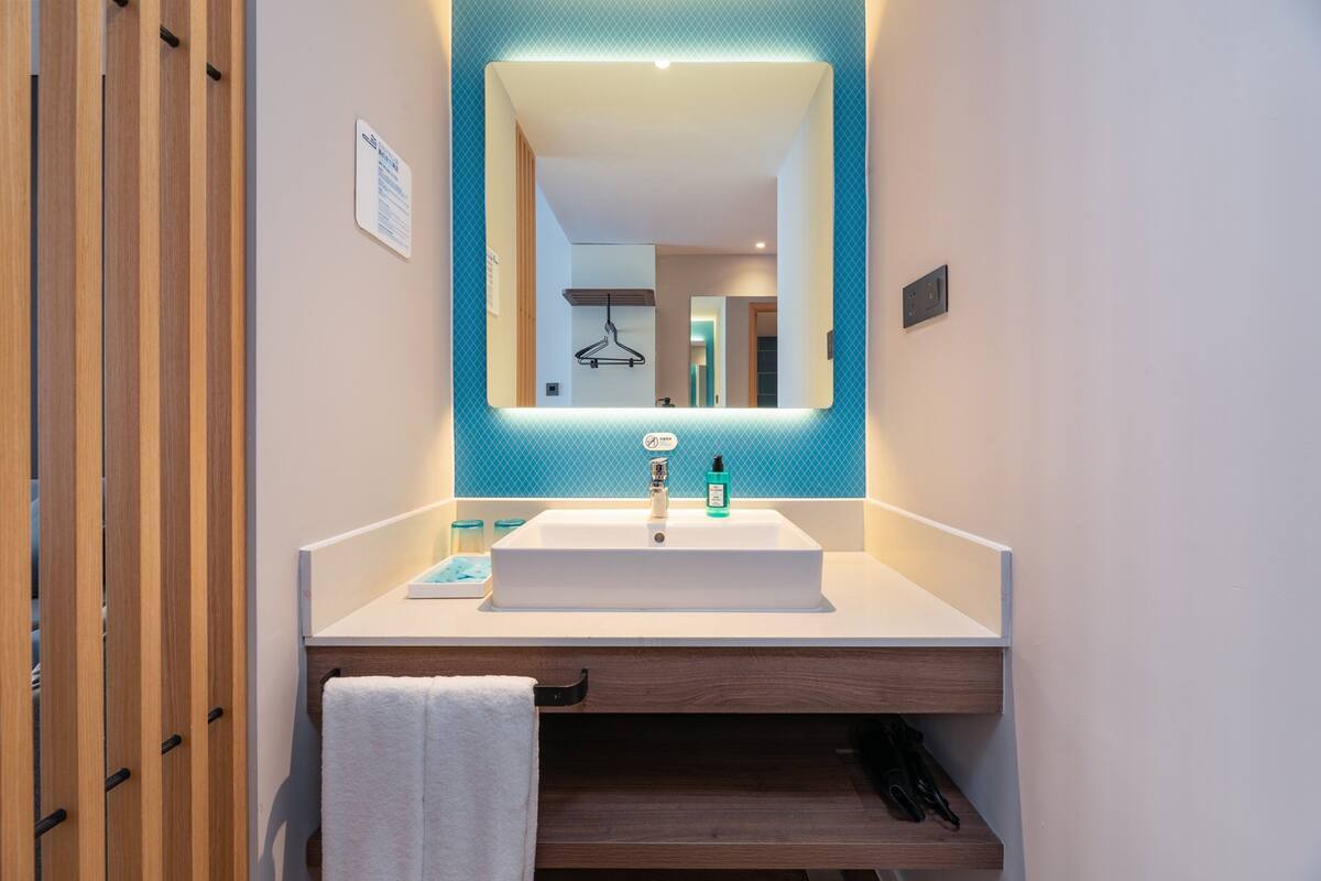 A modern bathroom with a large mirror, white sink, and wooden vanity.