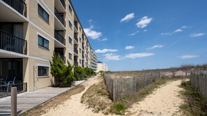 Un hôtel situé en bord de mer, doté d’une terrasse en bois, d’un sentier sablonneux et d’une clôture.