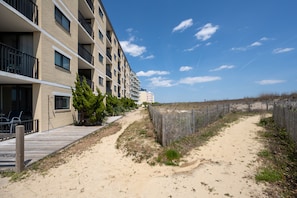 A beachfront hotel with a wooden deck, sandy path, and a fence.