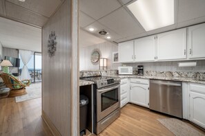 A modern kitchen with white cabinets, stainless steel appliances, and a wooden floor.