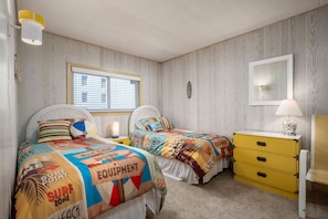 A bedroom with two beds, a nightstand, a dresser, and a window with blinds.