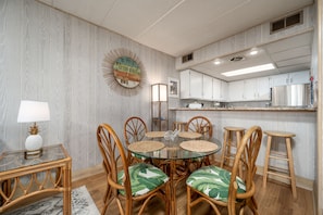 A dining area with a glass table, wicker chairs, and a tropical-themed cushion.