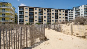 Un immeuble résidentiel à plusieurs étages doté de balcons, une plage de sable au premier plan et un ciel bleu dégagé.