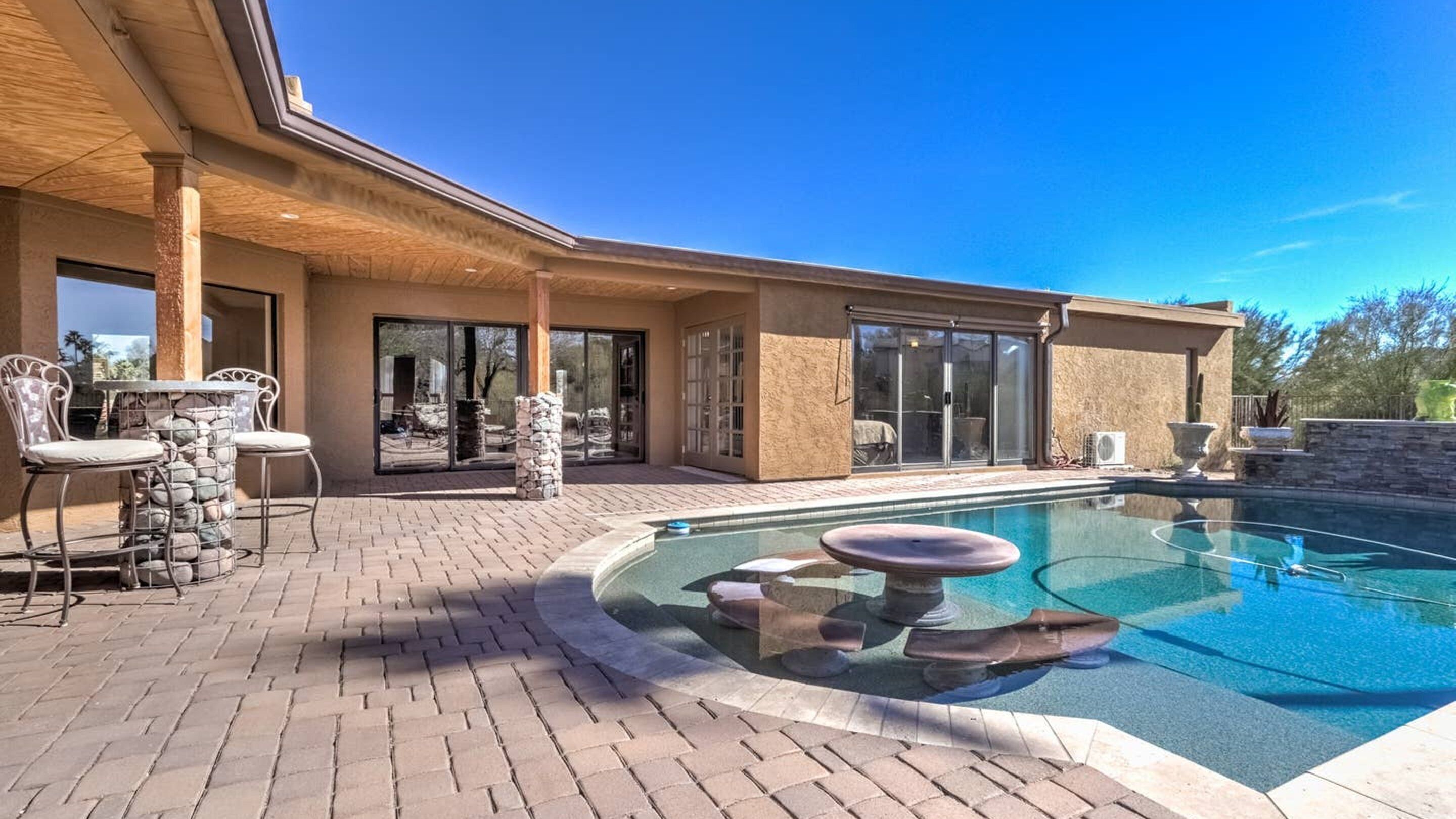 A modern house with a swimming pool, patio furniture, and a stone pillar.