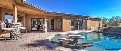A modern house with a swimming pool, patio furniture, and a stone pillar.
