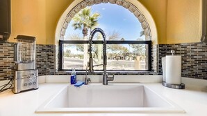 A kitchen with a white sink, a blender, a faucet, and a window with a view of palm trees and a street. - Fountain Hills Gem With Pool and Great Views! (Fountain Hills)