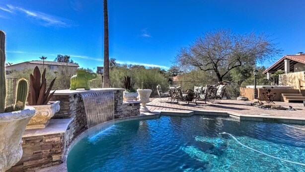 A swimming pool with a stone waterfall feature, surrounded by patio furniture and cacti. - Fountain Hills Gem With Pool and Great Views! (Fountain Hills)