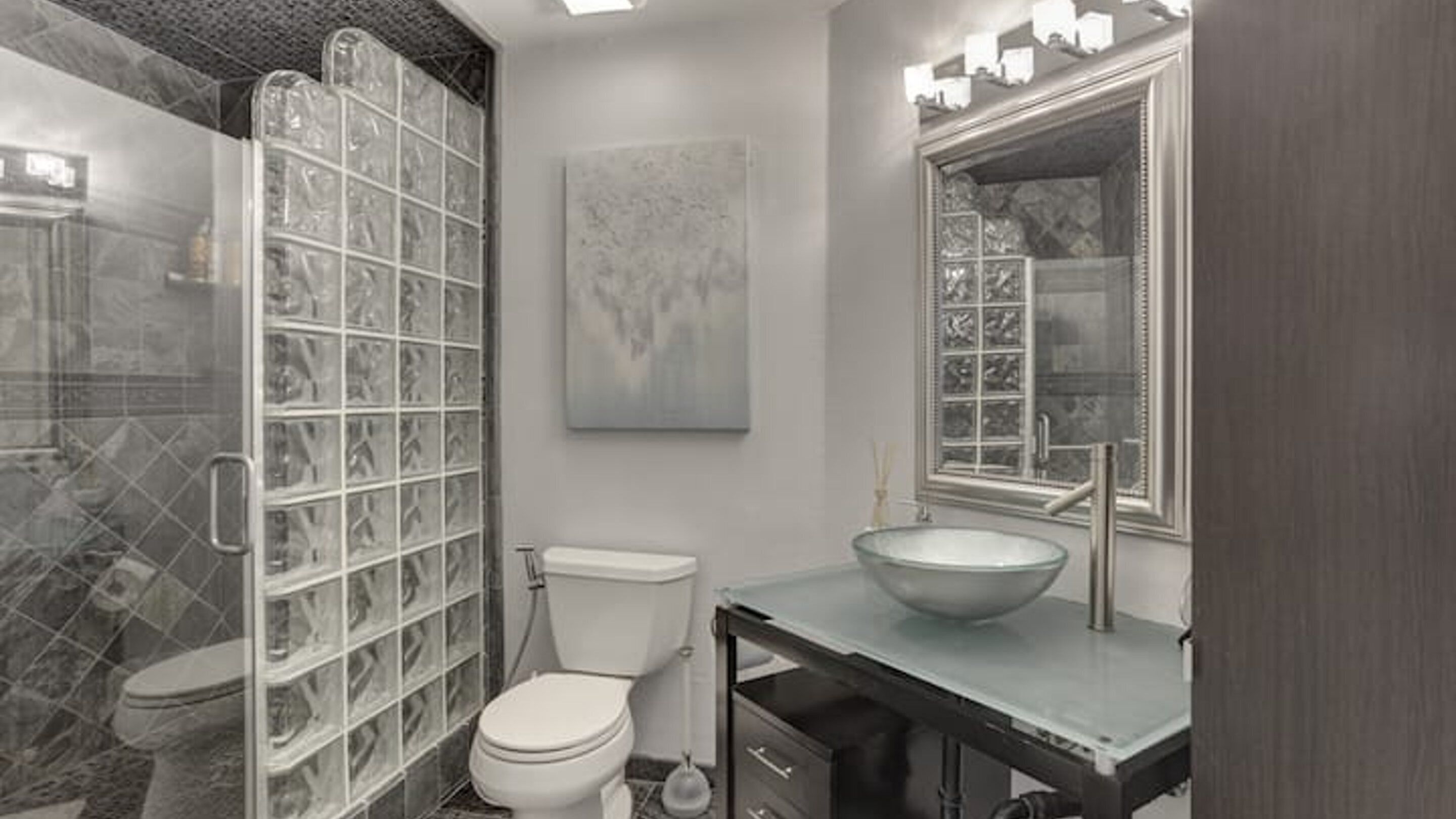 Une salle de bain avec une douche à parois de verre, des toilettes, un lavabo avec un grand miroir et un luminaire fixé au mur.