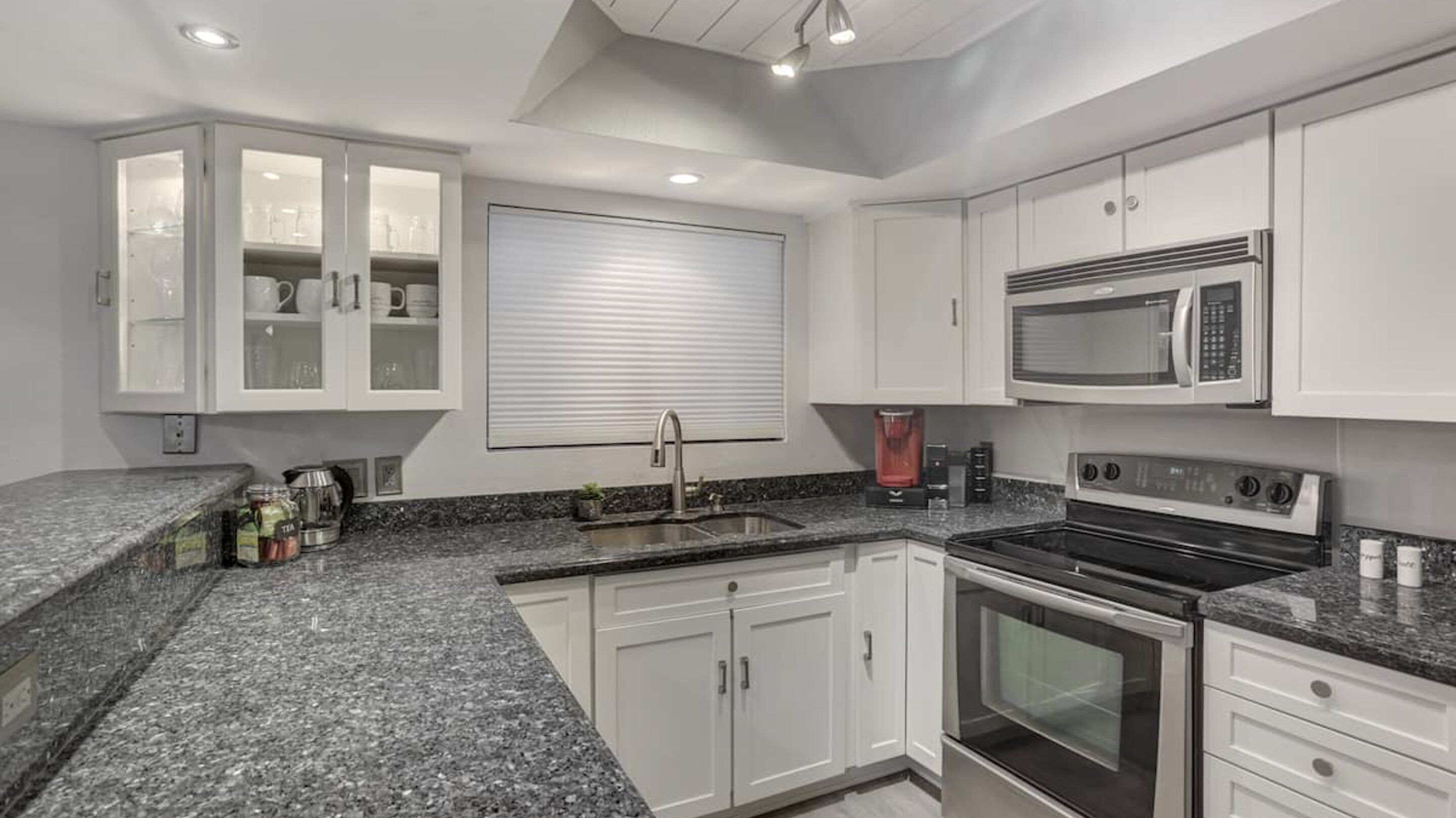 A modern kitchen with granite countertops, stainless steel appliances, and white cabinetry.