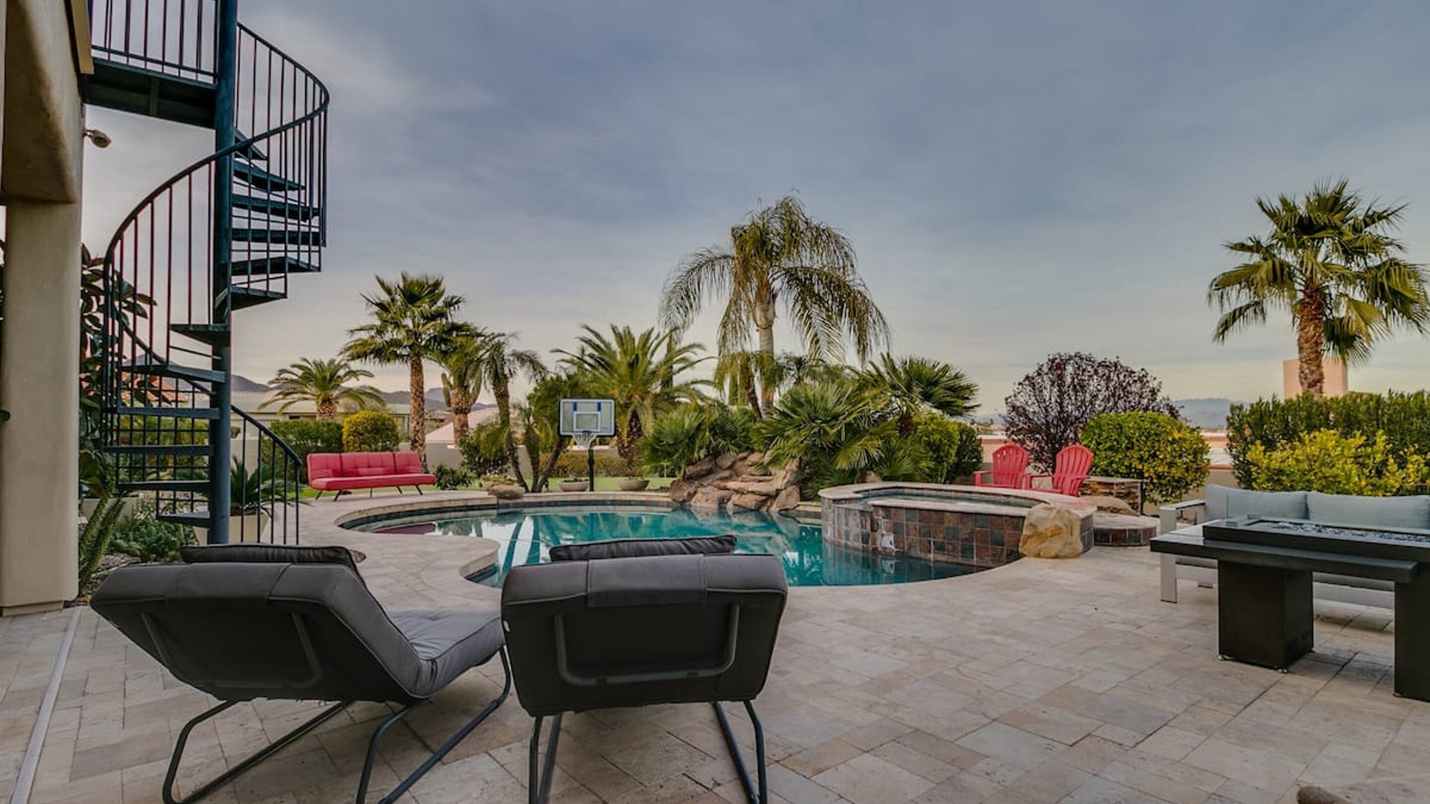 A pool area with a hot tub, lounge chairs, and a spiral staircase.