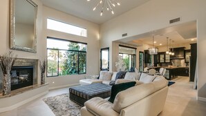 A spacious living room with a fireplace, large windows, and a modern kitchen in the background. - Luxury Contemporary Sanctuary w/ Pool and Views! (Fountain Hills)