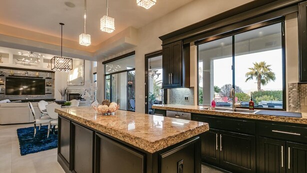 A modern kitchen with granite countertops, dark cabinetry, and large windows offering a view of palm trees. - Luxury Contemporary Sanctuary w/ Pool and Views! (Fountain Hills)