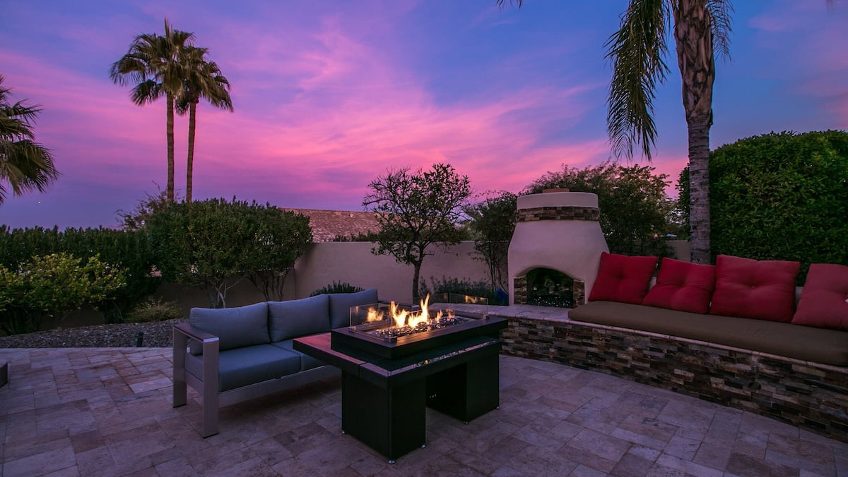 An outdoor patio with a fire pit, seating area, and a stone fireplace.
