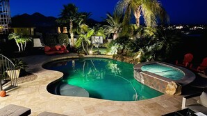 A swimming pool with a curved design, surrounded by palm trees and a red chair. - Luxury Contemporary Sanctuary w/ Pool and Views! (Fountain Hills)