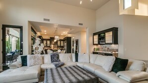 A spacious living room with a large sectional sofa, a dining area with a kitchen in the background, and a modern chandelier. - Luxury Contemporary Sanctuary w/ Pool and Views! (Fountain Hills)